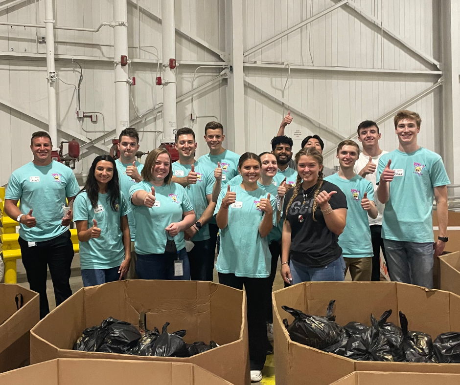 Michigan YPN Team in teal t-shirts in front of the food they packed